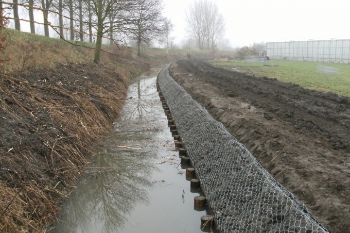 houten planken met palen en schanskorf op talud